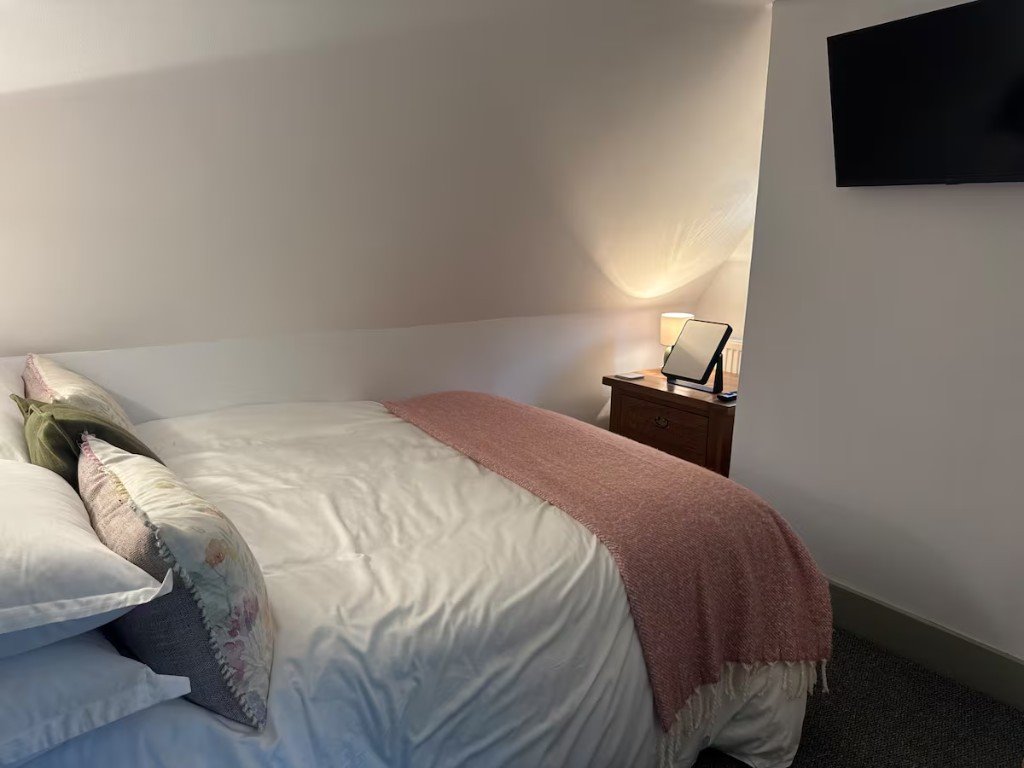 A third bedroom under the sloping ceiling, with a pink throw across the bed and a lamp on the bedside table