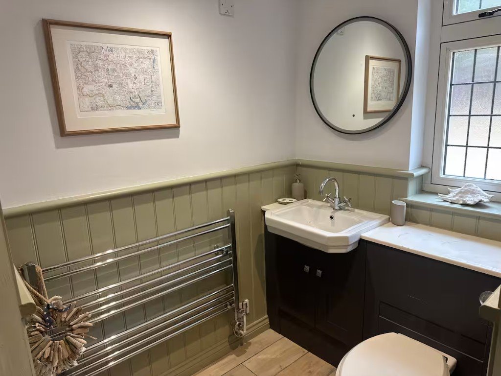 The downstairs bathroom, with sage panelling, a basin on a dark vanity unit and a framed map